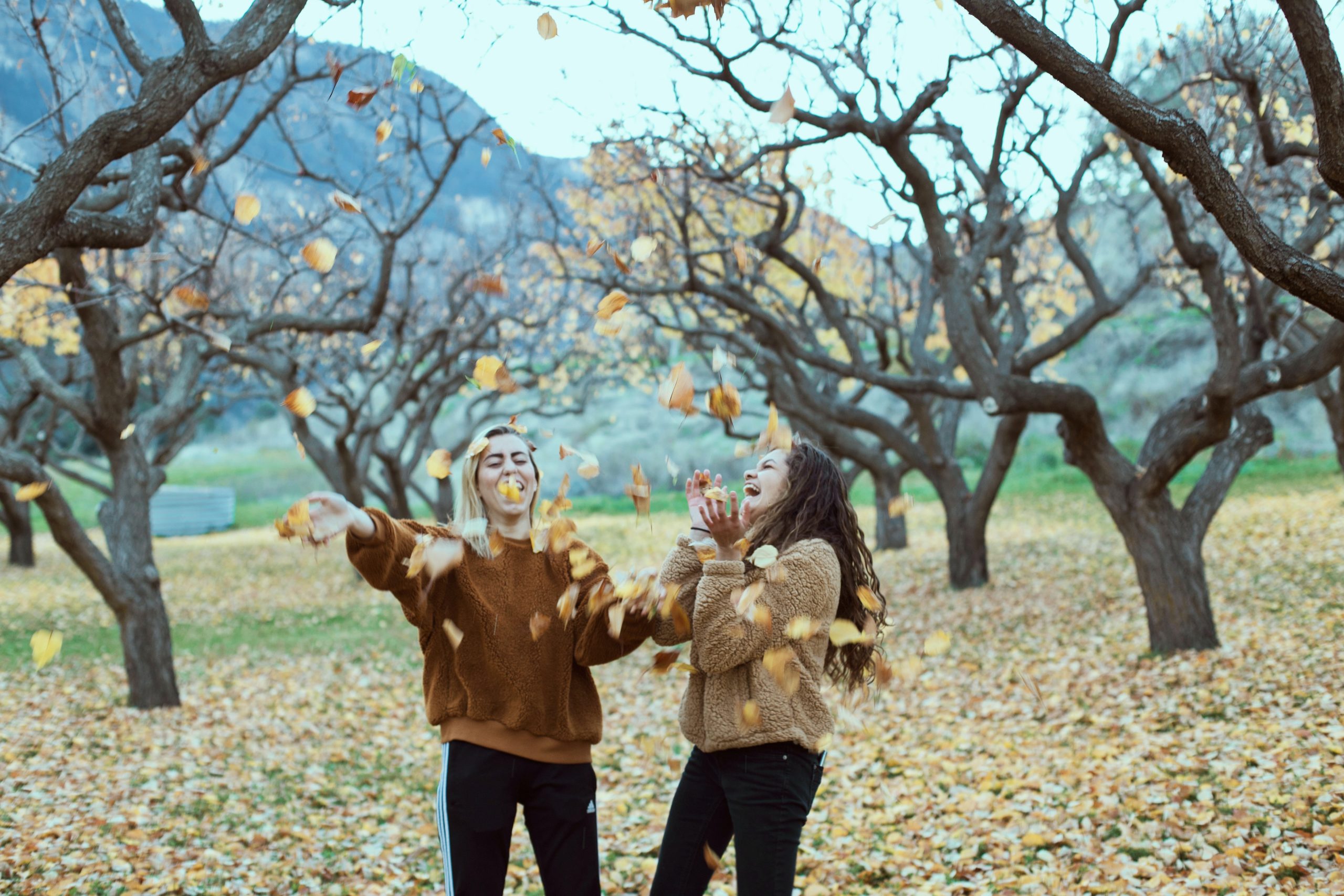 Two happy ladies throwing leaves in the air in a park
